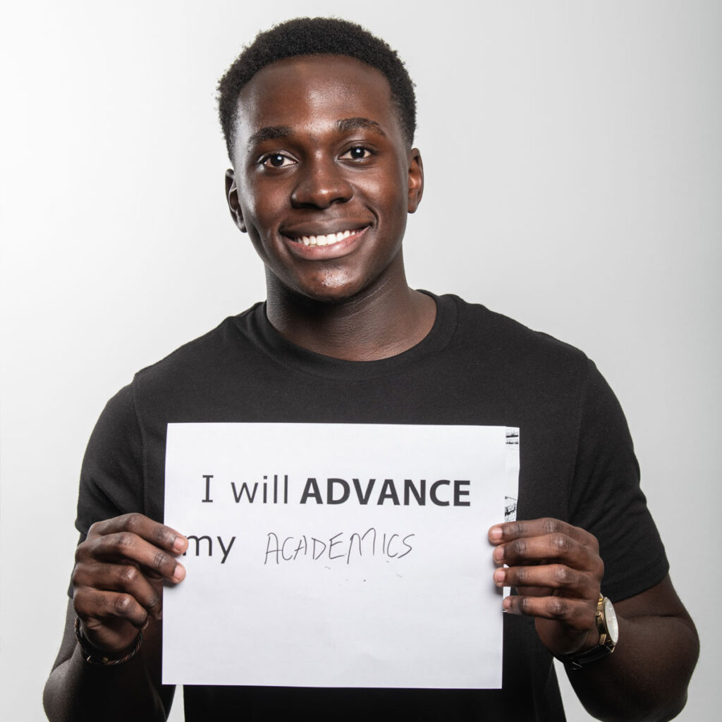 Male George Mason transfer student holding a sign with text written on it that says, "I will ADVANCE my academics"